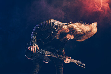 Emotional portrait of a rock guitar player with long hair and beard plays on the black background