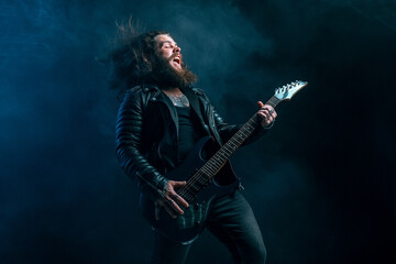 Fototapeta na wymiar Expressive rock male guitarist with long hair and beard plays on the smoke background. Studio shot