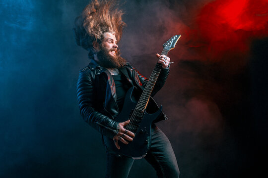 Expression rock guitar player with long hair and beard plays on the smoke background. Studio shot