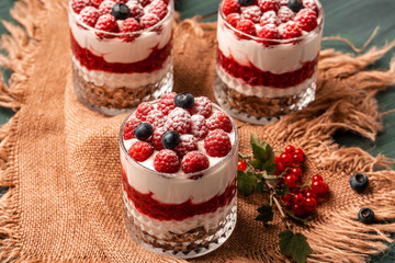 Healthy raspberry fruit dessert with skyr yogurt, granola layered in jar surrounded by ingredients, Vegetarian breakfast, fresh raspberries and blueberries yoghurt