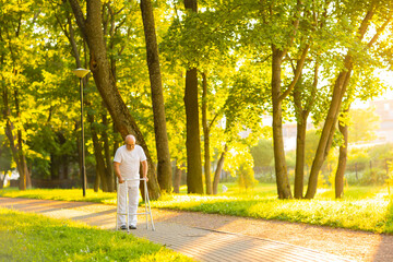 Old man is walking with walker outdoor at sunset. Rehabilitation concept.