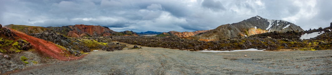 Beautiful panoramic Icelandic landscape of colorful rainbow volcanic Landmannalaugar mountains, at famous Laugavegur hiking trail with dramatic snowy sky, and red volcano soil in Iceland.