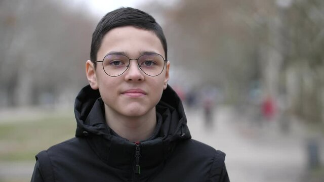 European boy 13 years old, stands on the street in autumn and looks towards the camera and smiles. Close-up, shallow depth of field