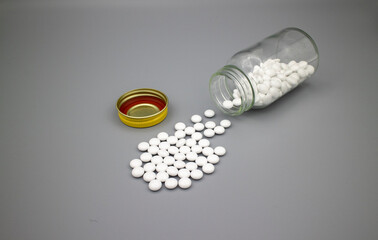 薬瓶からこぼれた白い錠剤、グレー背景 3
White tablets, medicaments, pills spread from the bottle on the gray surface.
