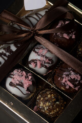 Candies in chocolate glaze. In a gift box. Tied with a ribbon tied into a bow. On a black background.