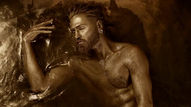 a man practices an ecstatic dance lying in the water in a trance state with golden skin.