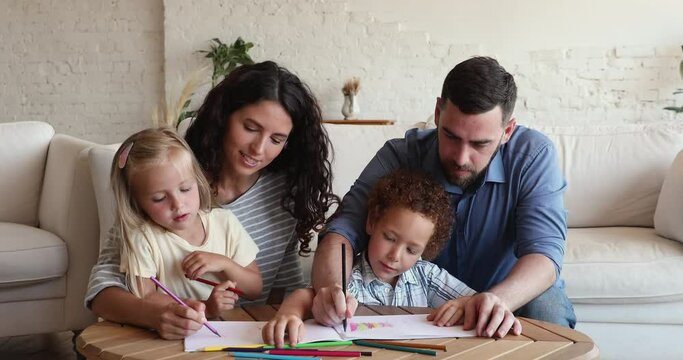 Multi ethnic full family gather together in living room drawing with colored pencils in paper album cozy at home. Weekend leisure, good creative hobby of kids and parents, unity and upbringing concept