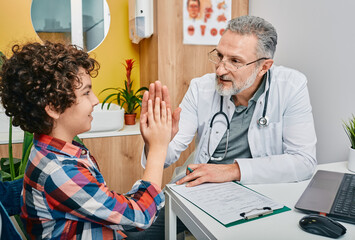 Friendly pediatrician having fun with her child patient at doctor's office and gives five for boy....