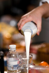A bottle of milk in a man's hand. Milk is poured into glassware.