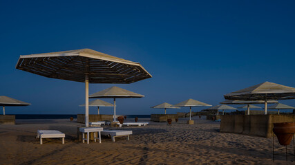 Overnight on the Red Sea beach. Lattice sun umbrellas on the background of a deep blue sky. Empty sun beds and clay urns on the sand. There is no one. Egypt