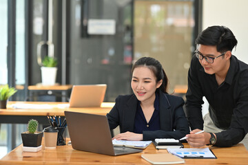 Photo of a businessman briefing job to office girl at the wooden table surrounded by a computer laptop and various office equipment.