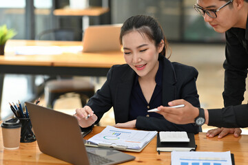 Photo of a businessman briefing job to office girl at the wooden table surrounded by a computer laptop and various office equipment.