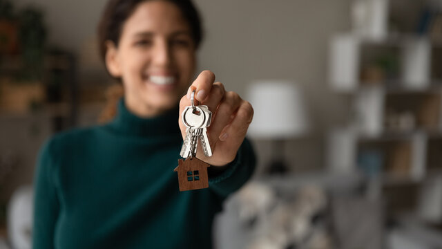 Close up young happy blurred woman showing keys to camera, feeling excited of purchasing own apartment or moving into new renovated dwelling, real estate agency professional service or tenancy concept