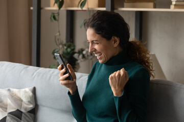 Overjoyed happy young hispanic woman looking at telephone screen, getting amazing victory news,...