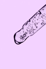 Transparent pipette with cosmetics on a purple background.