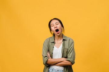 Portrait of Young Asia lady with negative expression, bored yawning tired covering mouth with hand in casual clothing isolated on yellow background with blank copy space. Facial expression concept