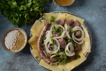Beshbarmak - National Kazakh dish, prepared with meat and pasta. Beshbarmak dish close-up on a plate on the table. Large pieces of stewed meat and onion