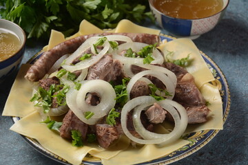 Beshbarmak - National Kazakh dish, prepared with meat and pasta. Beshbarmak dish close-up on a plate on the table. Large pieces of stewed meat and onion