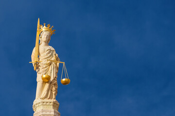 Lady Justice holding balance scales and sword, a 15th century medieval statue at the top of St Mark Basilica in Venice (with blue sky and copy space)