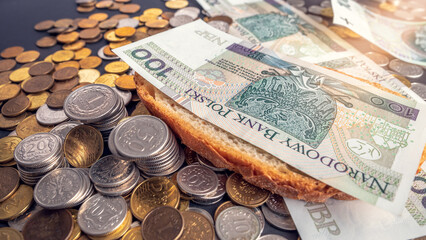 PLN 100 banknote placed on a slice of bread. Difficult financial situation in Poland. Inflation consuming our savings. A slice of bread lying on Polish banknotes and coins.