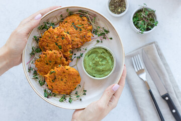 female hands holding plate with vegan sweet potato fritters and creamy avocado dip over blurred kitchen table. Vegan lunch plate. closeup