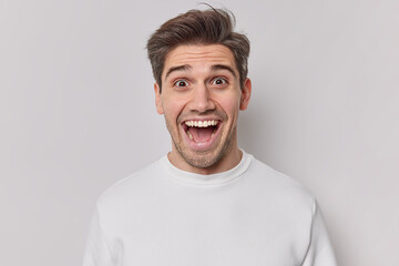 Portrait of happy cheerful guy keeps mouth opened reacts on amazing news glad to hear something pleasant dressed in casual jumper isolated over white background. Emotions and reactions concept