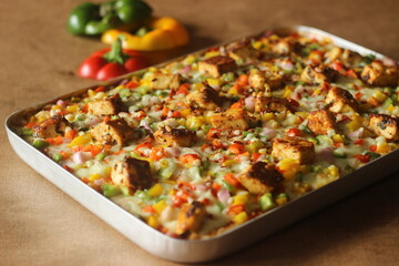 Home baked pizza loaded with paneer, mozzarella cheese, red yellow green capsicums. Baked in a rectangular tray