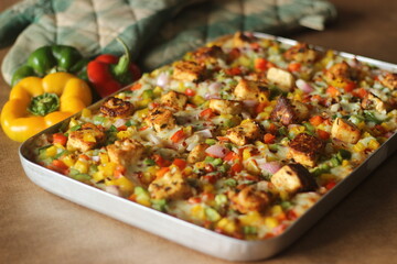 Home baked pizza loaded with paneer, mozzarella cheese, red yellow green capsicums. Baked in a rectangular tray