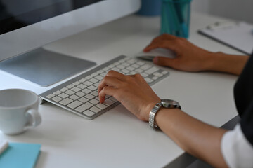 Cropped image of woman hand typing on a wireless keyboard and using wireless mouse at the white modern working desk.