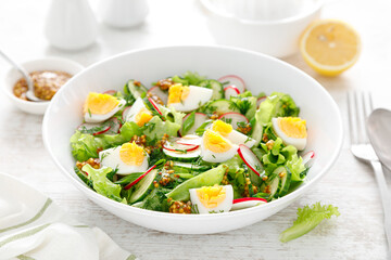Easter fresh vegetable salad with boiled egg, radish and cucumber, dressing with dijon mustard and lemon on white wooden table