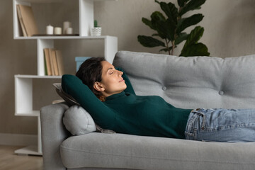 Obraz premium Relaxed young attractive hispanic latina woman lying on comfortable sofa, seeing sweet dreams, sleeping or napping, breathing fresh air, enjoying carefree peaceful weekend alone in living room.