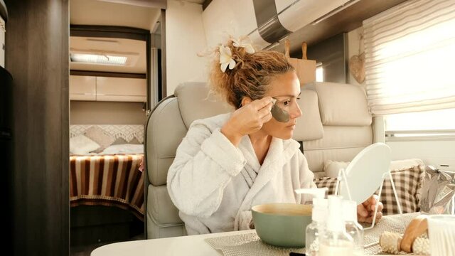 Caucasian woman making beauty skin treatment using cream and mirror sitting and relaxing inside a camper van in travel vanlife lifestyle. Adult female people have care and use mask for aging