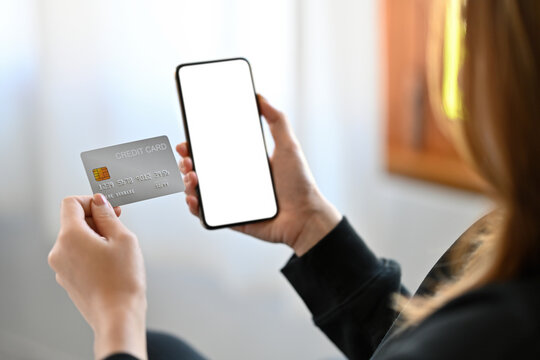 Cropped image of a businesswoman holding a white blank screen mobile and credit card in the modern living room.