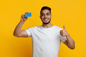 Cheerful middle eastern man showing credit card and thumb up