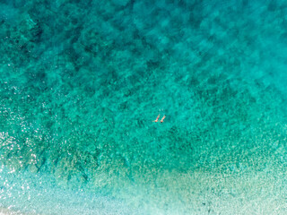 Aerial drone view of swimmers in the sea at summer. Tourists diving and swimming in the water. Transparent sea water in bay. 