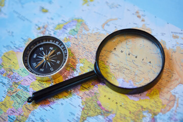 The magnifying glass is located on the world map and magnifies the country of Russia. There's a compass next to it. Concept of travel in the selected country.