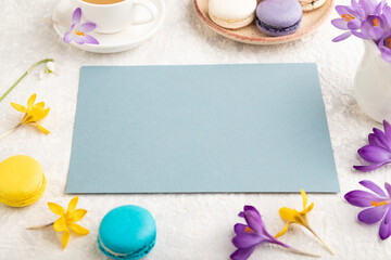 Blue paper sheet mockup with spring snowdrop crocus flowers and multicolored macaroons on gray concrete background. side view, copy space.