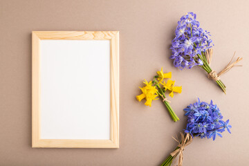 Wooden frame with spring snowdrop flowers bluebells, narcissus on beige pastel background. top view, copy space, mockup, template.