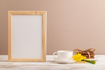 Wooden frame with oatmeal cookies yellow narcissus and coffee cup on beige pastel background. side view, copy space.