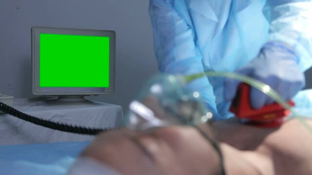 Doctor in operating room trying to help on intensive care patient, use defibrillator electrical device to shock heart. Looks at the monitor with vital data. Green Screen