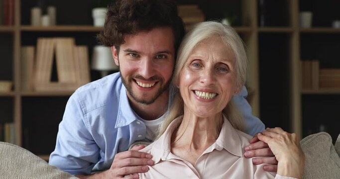 Close up head shot older grey-haired woman her young adult 35s son smile looking at camera, pose at home, having good friendly relations, enjoy bond and love. Multigenerational family portrait concept