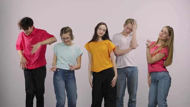 A group of cute young people looking at the camera and having fun dancing and having fun. Two guys and three girls models posing on a white background in the studio. Close up. Slow motion.