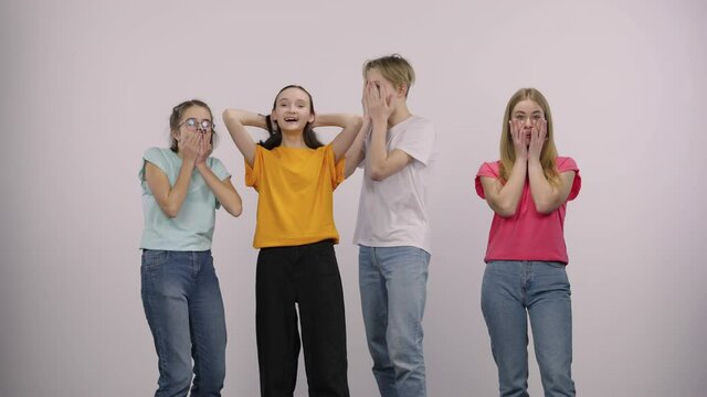 A group of cute young people looking at the camera with surprise and wow delight, then dancing and having fun. Guy and three girls models posing on a white background in the studio.
