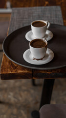 two mugs of coffee stands on a tray in a restaurant.  dark colors, loft style interior.  no people