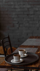 two mugs of coffee stands on a tray in a restaurant.  dark colors, loft style interior.  no people