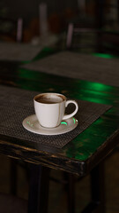 a mug of coffee stands on a tray in a restaurant.  dark colors, loft style interior.  no people