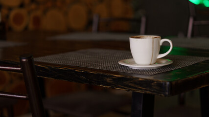 a mug of coffee stands on a tray in a restaurant.  dark colors, loft style interior.  no people