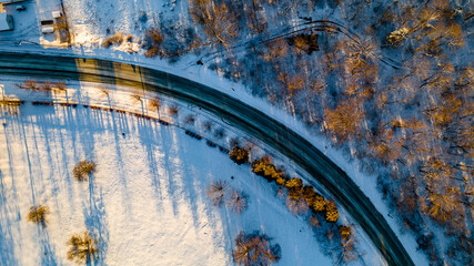 Drone photo of the bend of the road leading through the frosty winter forests and groves covered with the first snow