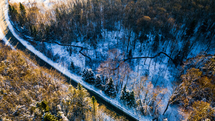 Drone photo of the bend of the road leading through the frosty winter forests and groves covered...