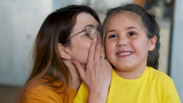 Mom and daughter are happy family. Girl whispers secret to her mother in her ear. Mom communicates with her daughter. Happy family concept. Mom whispers a secret in girl ear. Family games and fun.